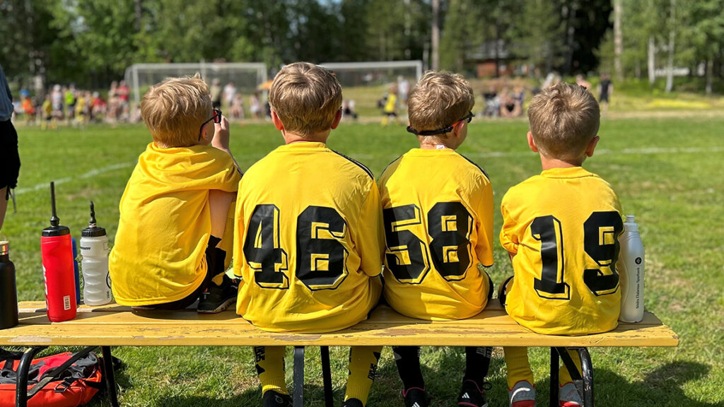 Fotbollskillar i gula matchtröjor på avbytarbänken.