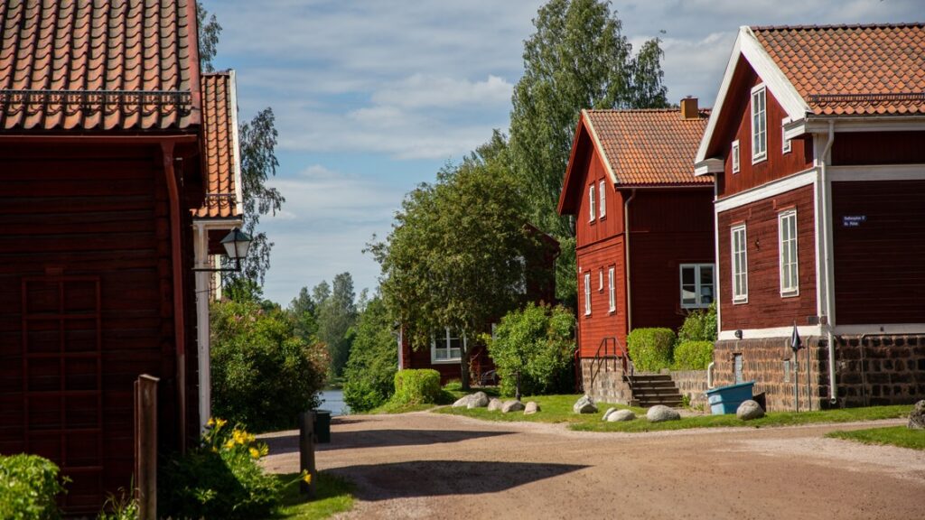 Röda timmerstugor längs en grusväg.